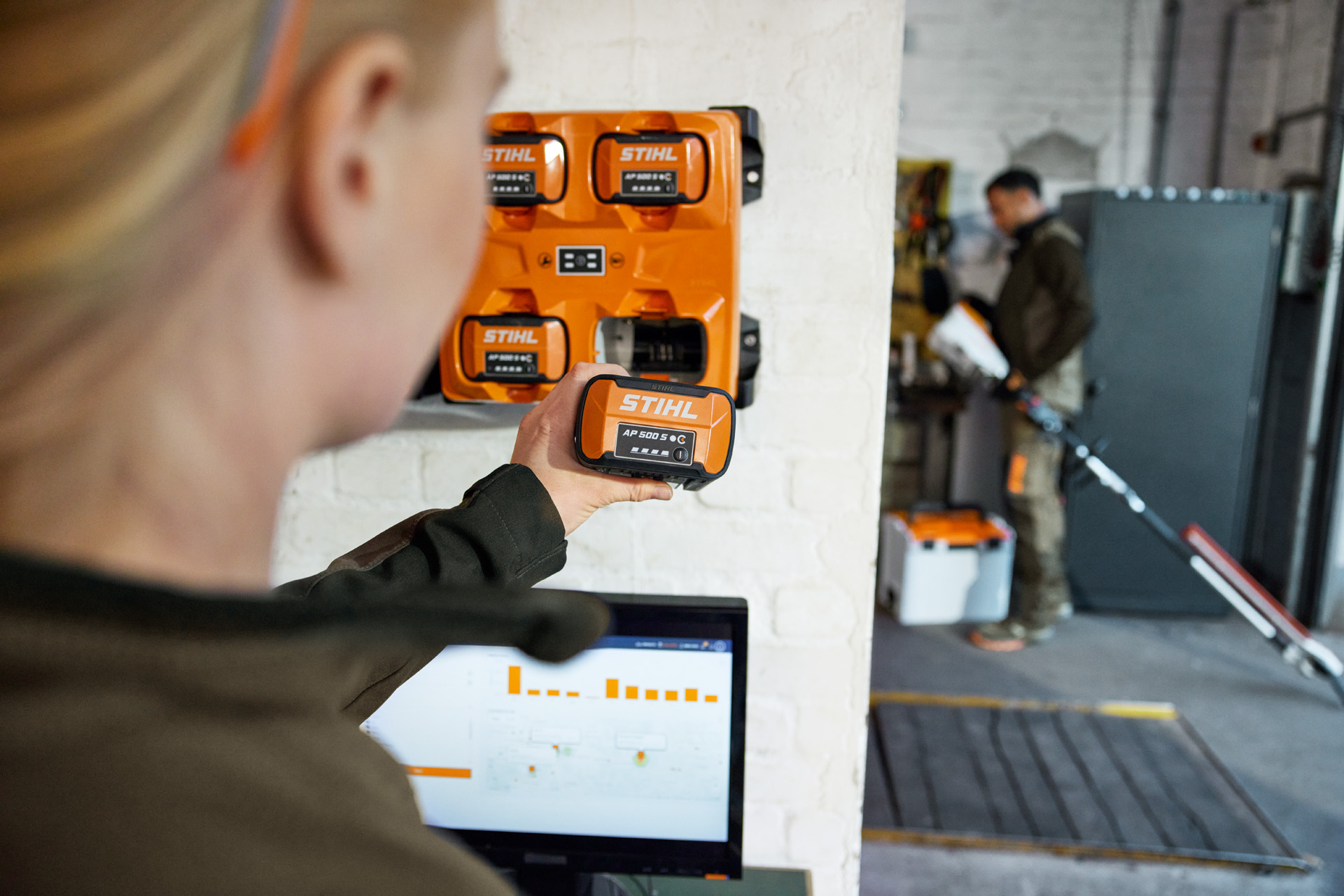 Una mujer delante de un portátil extrae un AP 300 S del cargador múltiple STIHL AL 301-4